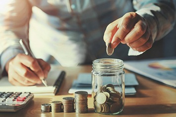 Man dropping a coin into a mason jar while writing down numbers