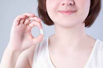 Nose-to-chest view of a girl in a white tank top holding up her extracted tooth